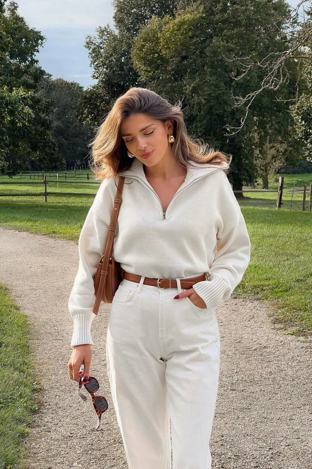 Stilvoller cremefarbener Pullover mit Reißverschluss, kombiniert mit hoch taillierter Jeans und braunem Gürtel – eleganter Look von Aphrodite™.