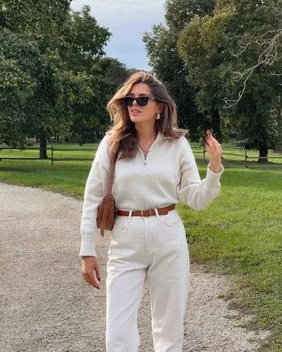 Stilvoller cremefarbener Pullover mit Reißverschluss, kombiniert mit hoch taillierter Jeans und braunem Gürtel – eleganter Look von Aphrodite™.